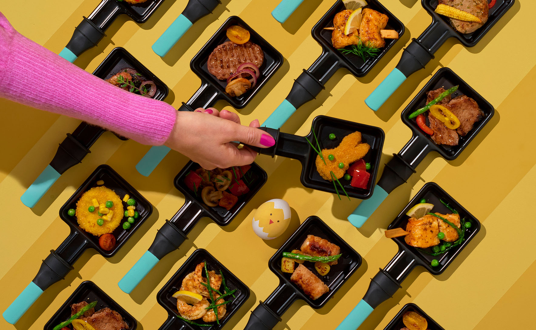 kleurrijk beeld van een hand die een gourmetpannetje oppakt van de tafel, getoond in bovenaanzicht