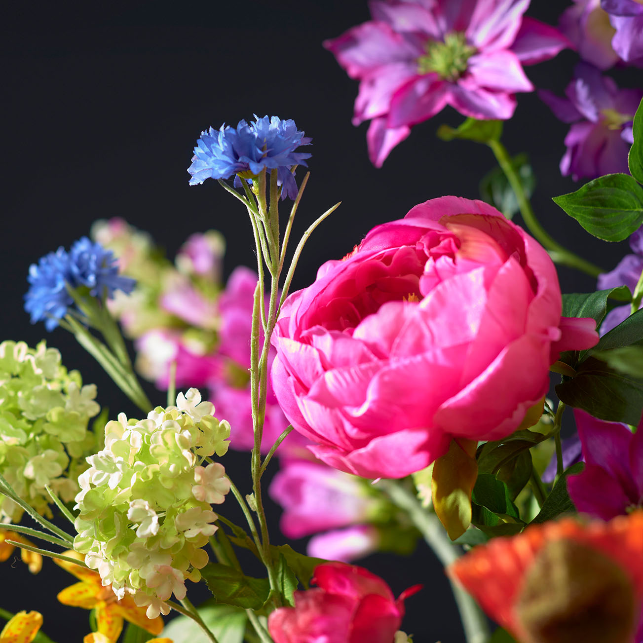 Close-up van delicate kleurrijke zijden bloemen gemixt boeket, gefotografeerd tegen een donkergrijze achtergrond. De bloemen zijn gedetailleerd weergegeven, waardoor hun textuur en natuurlijke uitstraling goed tot hun recht komen.