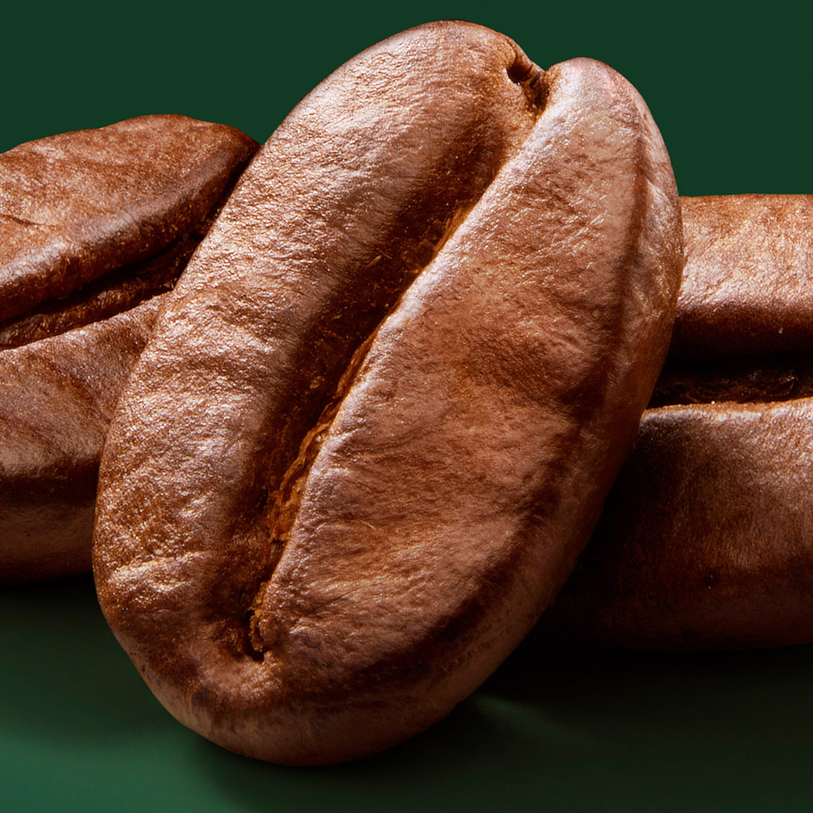 Extreme close-up of 3 well-lit, attractively looking coffee beans against a dark green background